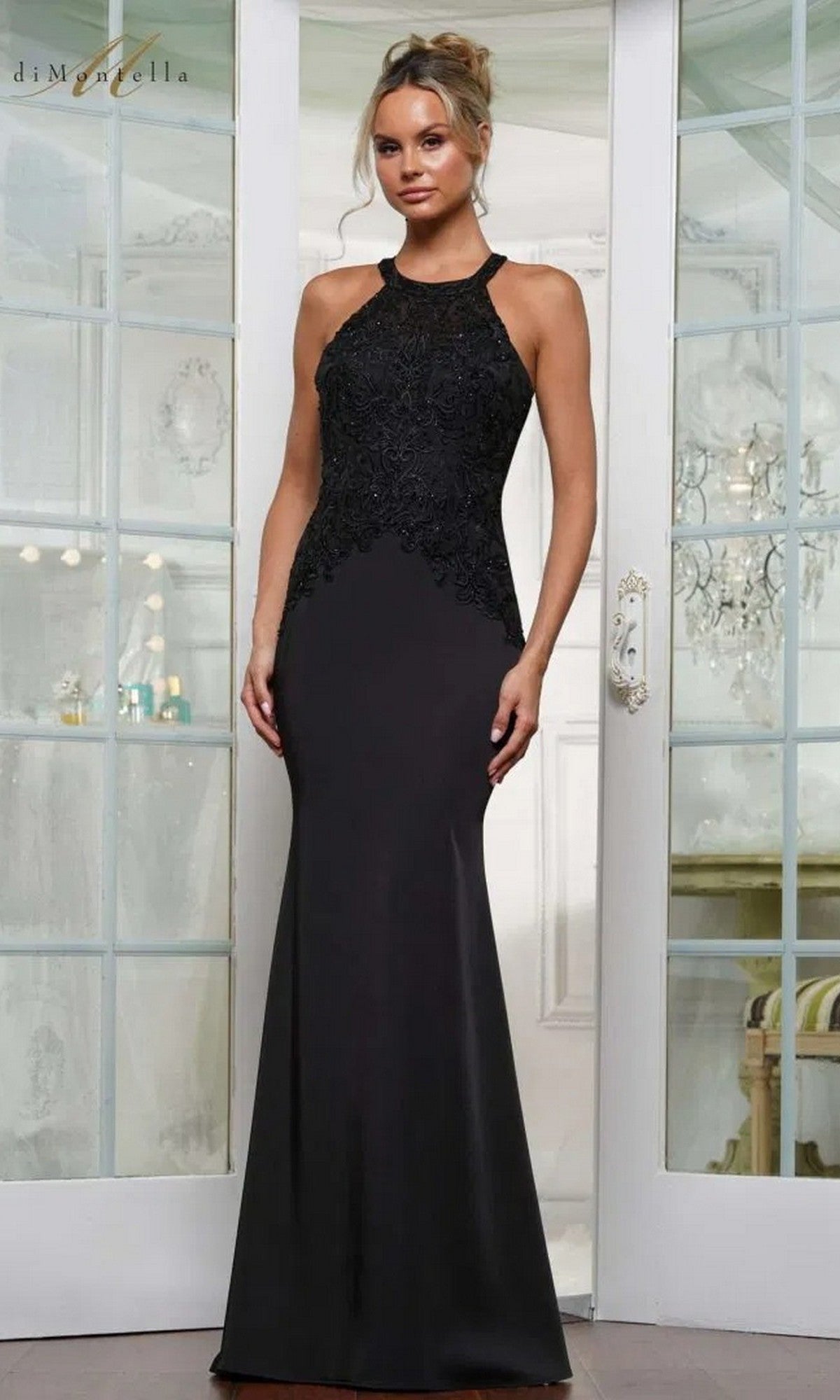 A woman poses indoors in the Rina Di Montella RD2755 long formal dress, featuring a sleeveless design and embroidered lace bodice, in front of glass-paneled doors.